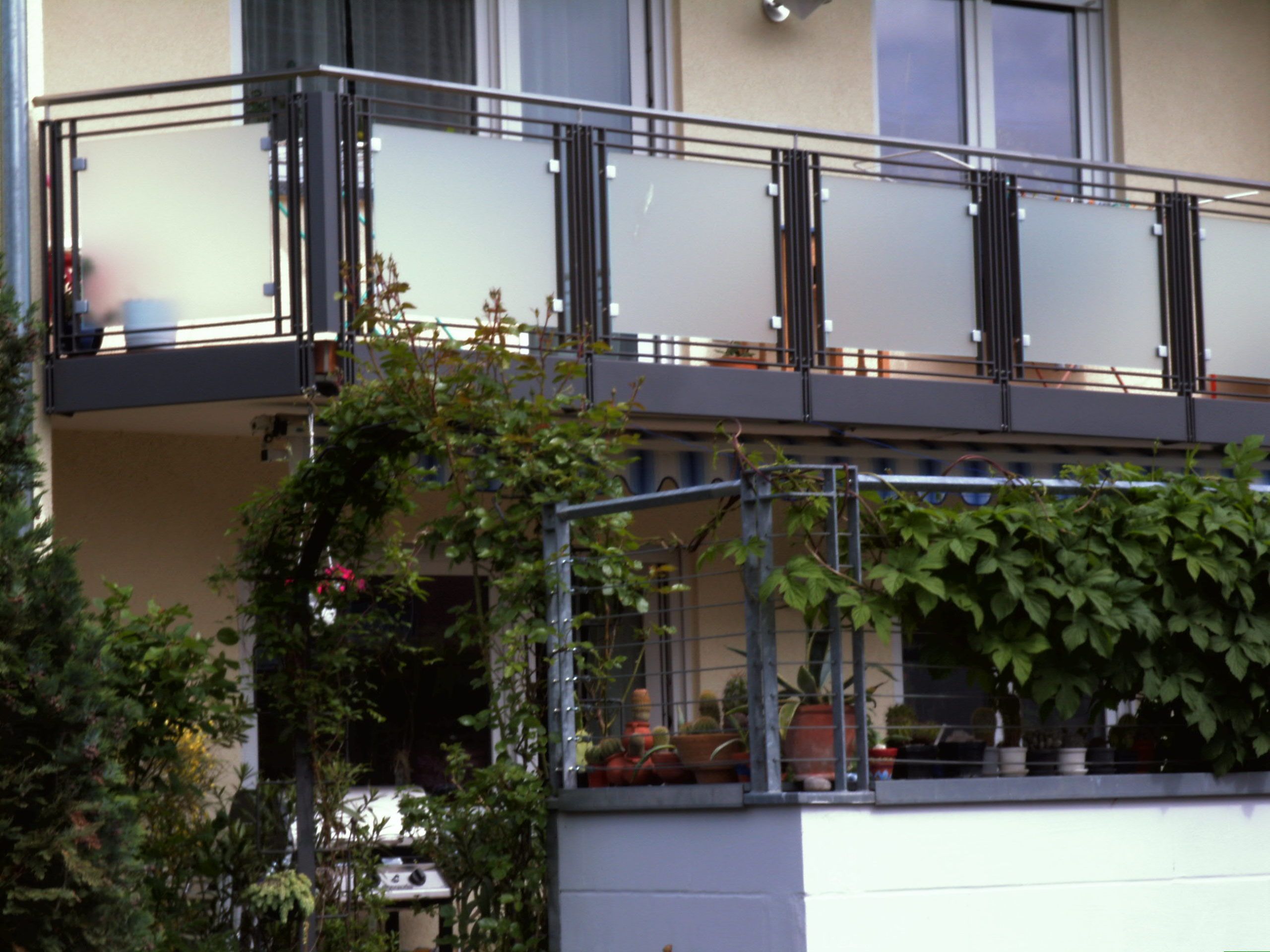 Balkongeländer aus schwarzen Metallstreben und Milchglas Platten 