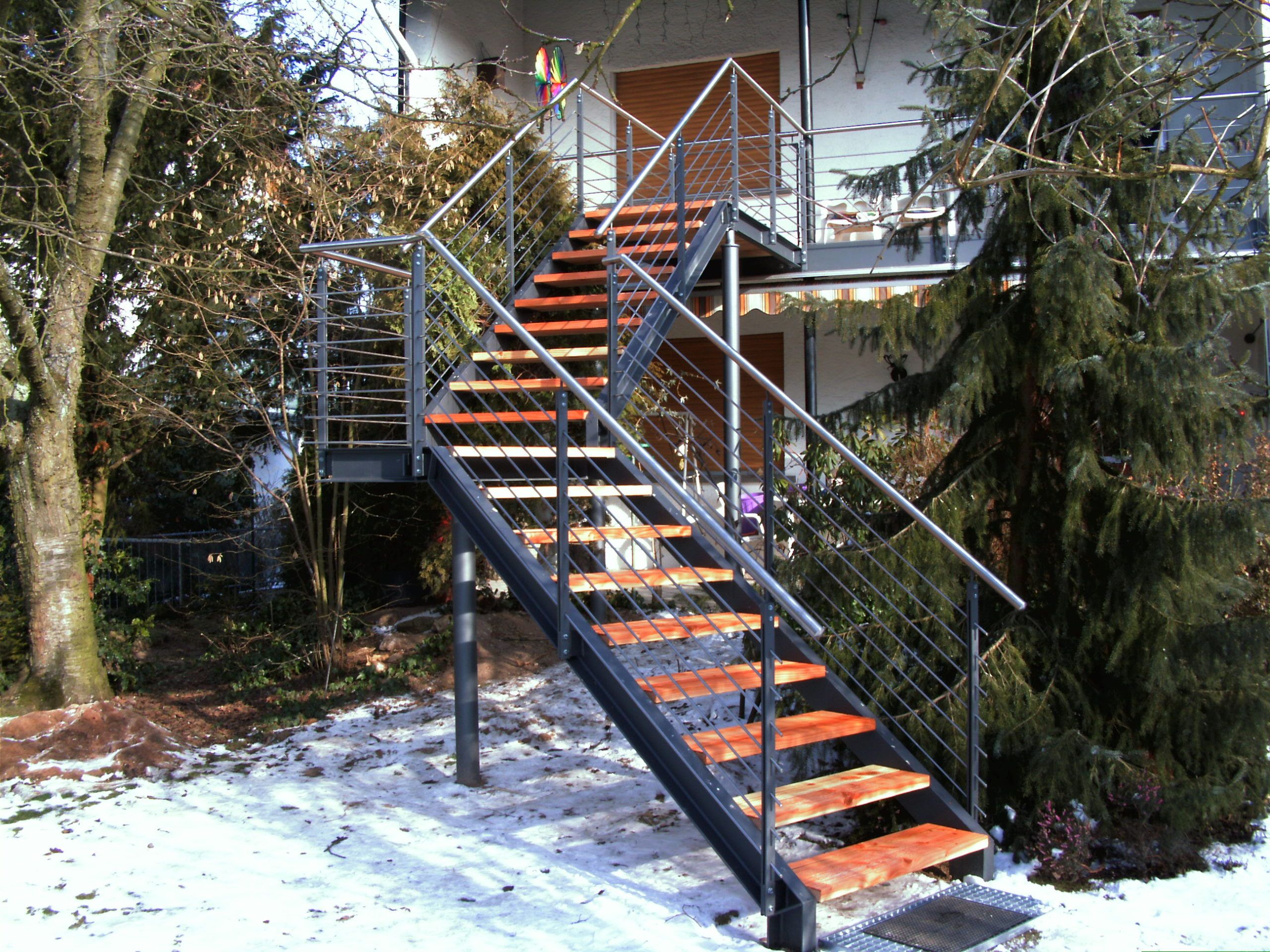 Holzstufen mit schwarzer Umrandung und Geländer aus Metallrundstäben mit einem grauen Metallhandlauf 