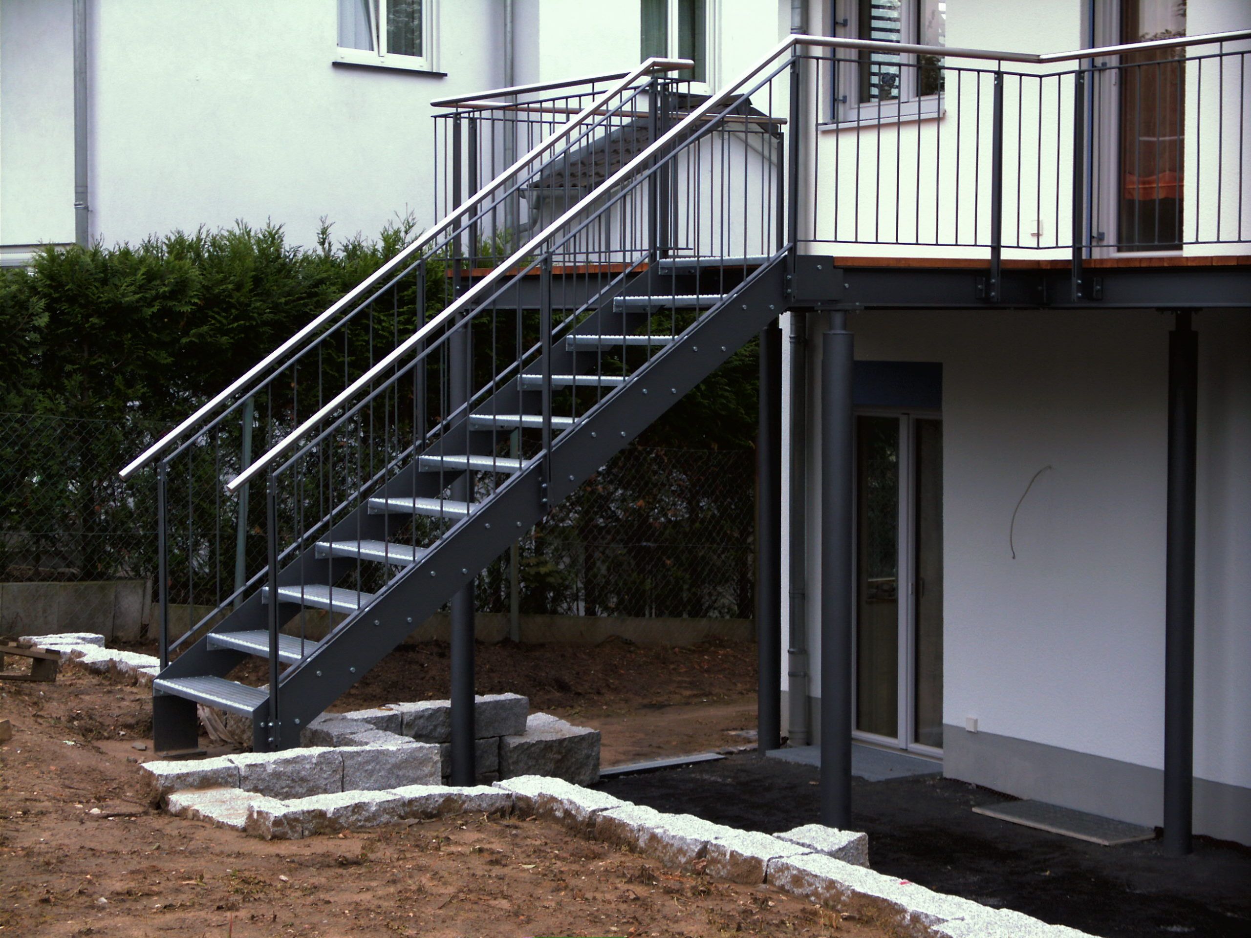 Stufen aus schwarzem Metallgitter mit schwarzer Umrandung und Geländer aus Metallstreben mit einem Metallhandlauf 
