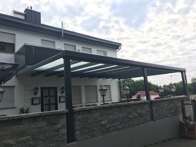 Carport aus schwarzen Metallstreben und mit einem Glasdach
