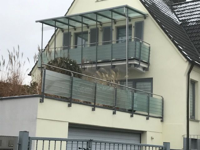 Balkongeländer aus blauem Milchglas und grauen Metallteilen  mit Dach