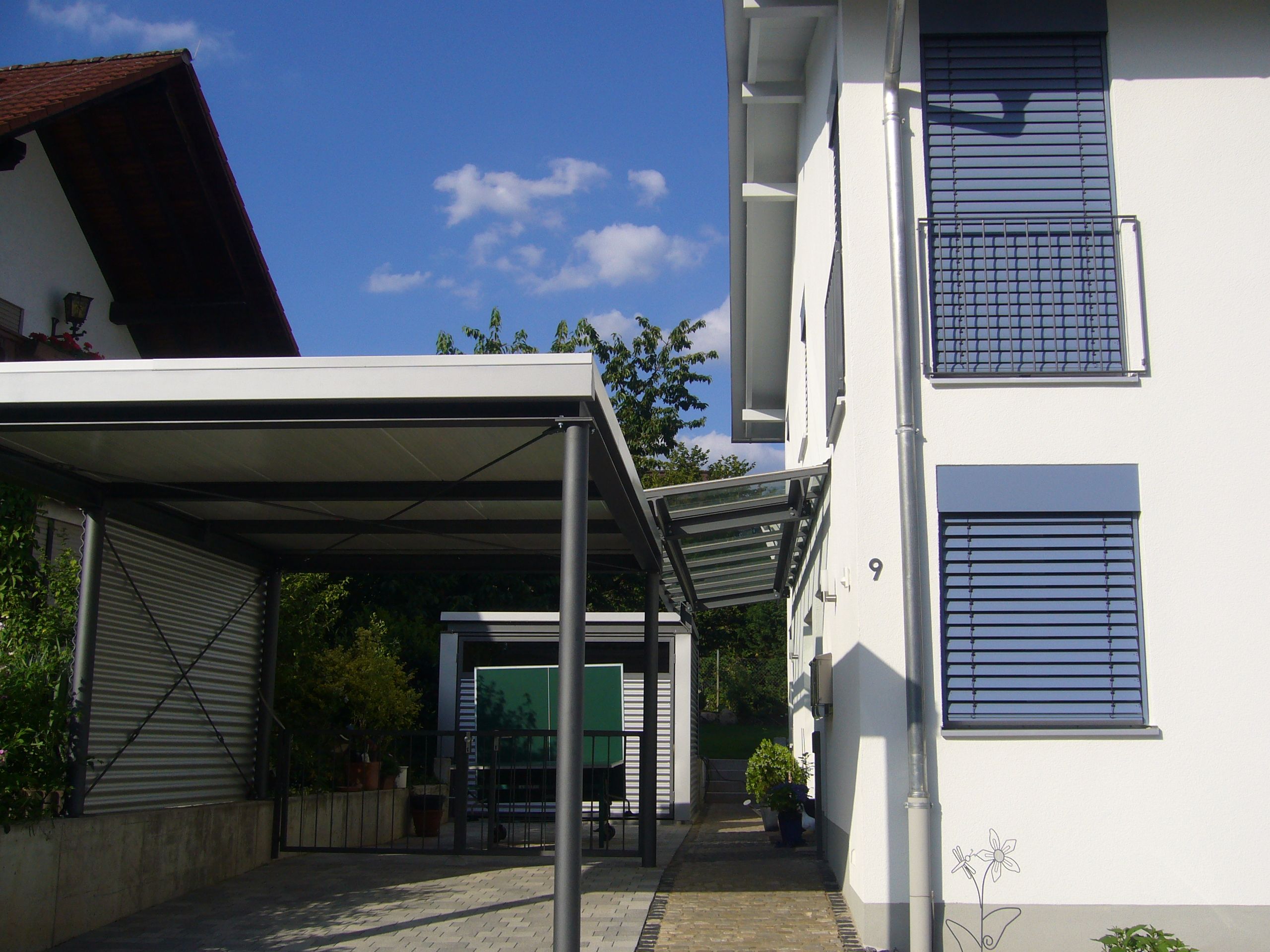 Carport aus dunklen Metallrundstäben als Stütze und einem weißen Dach 