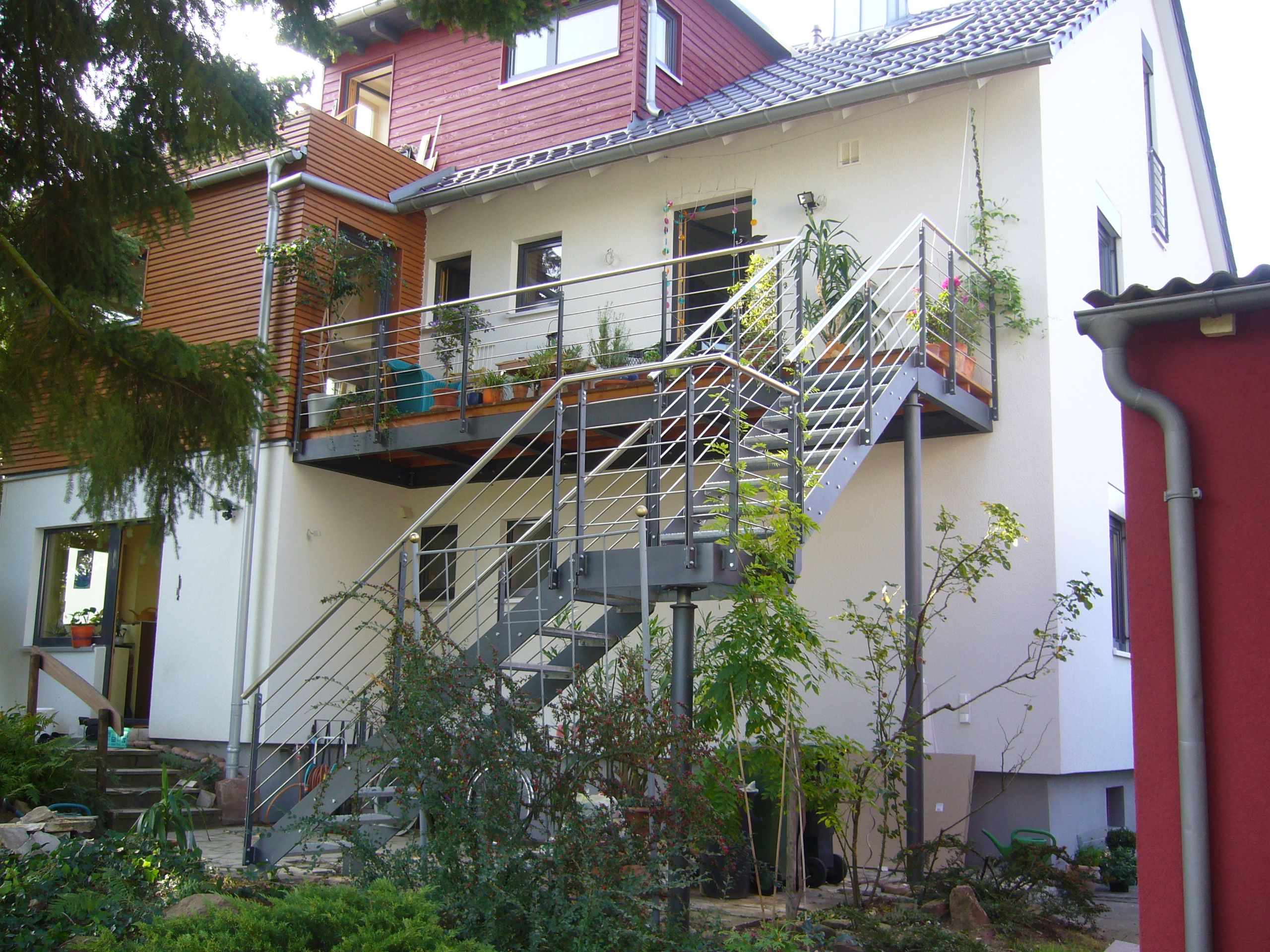 Stufen aus grauem Metallgitter mit schwarzer Umrandung und Geländer aus Metallrundstäben mit einem Holzhandlauf 