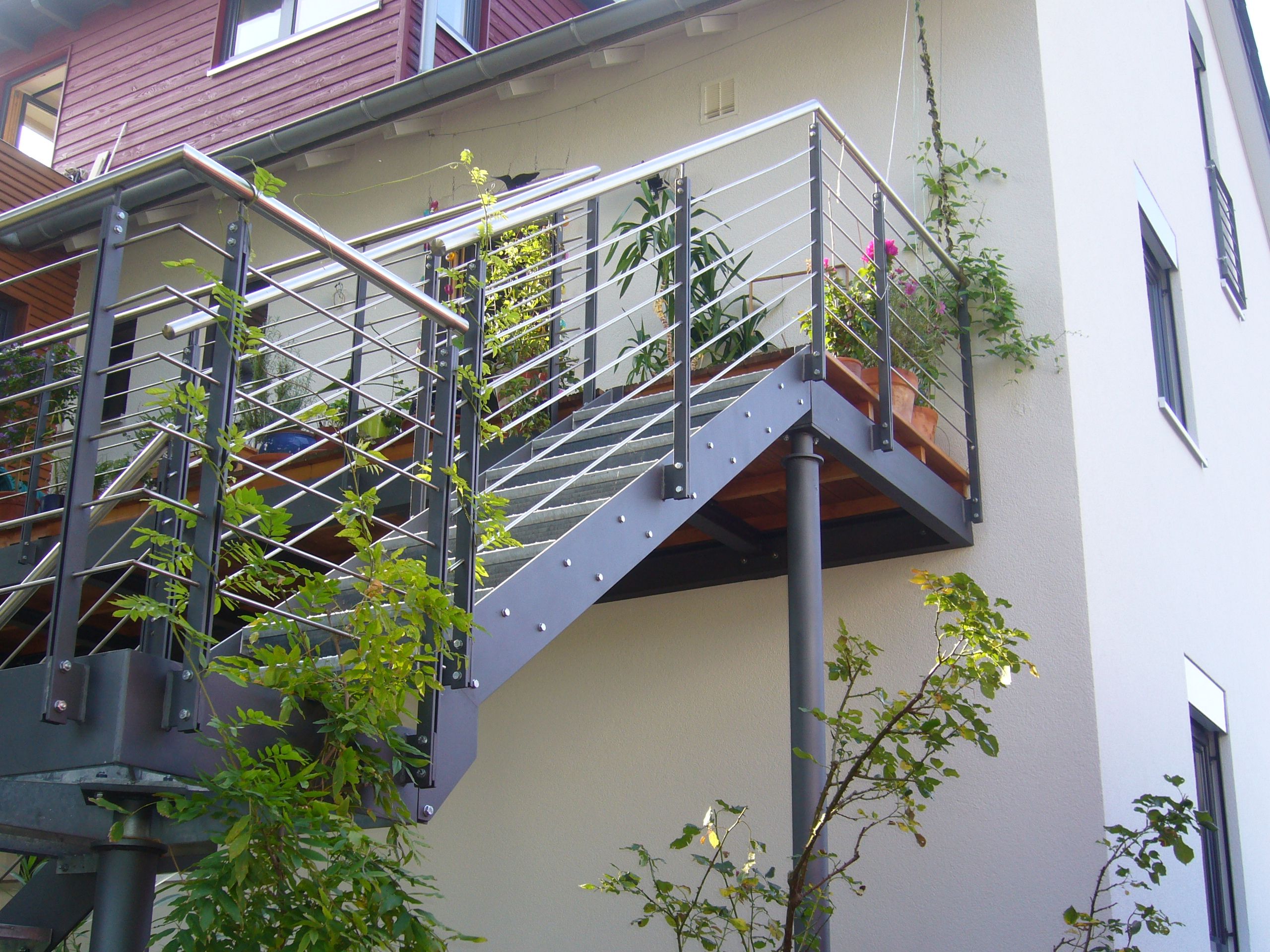 Stufen aus grauem Metallgitter mit schwarzer Umrandung und Geländer aus Metallrundstäben mit einem Holzhandlauf 